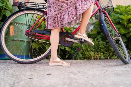 Close up on woman's legs female standing beside the bicycle wearing summer dress in a sunny dayの写真素材
