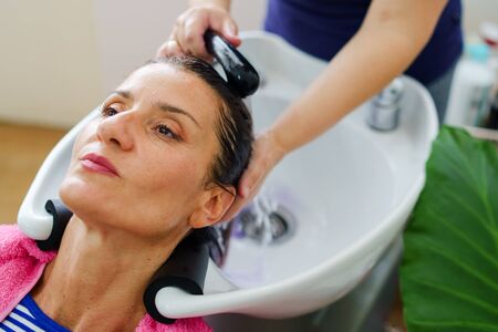 Hairdresser washing hair of woman female customer with a shower at the saloon applying shampoo on wet hairの写真素材