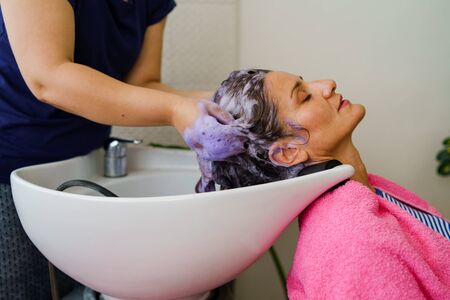 Hairdresser washing hair of woman female customer with a shower at the saloon applying shampoo conditioner on head hairの写真素材