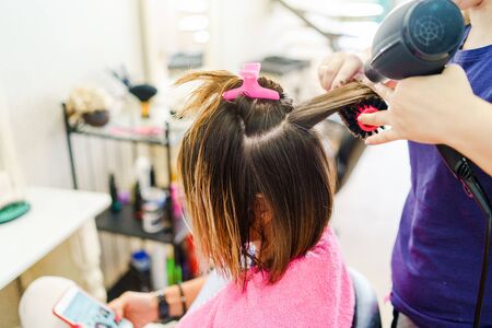 Professional female hairdresser drying woman's hair styling using blow dryer at the hairdressing saloonの写真素材