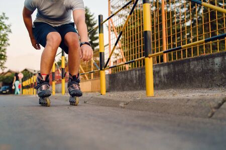Young man on roller blades skates riding by the fence wall looking waiting in a summer day evening rollerblading on the streetの写真素材