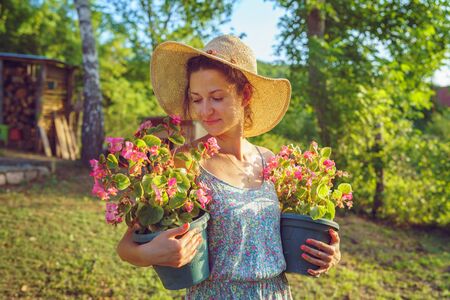 Young woman female farmer happy smiling carry two pots with flowers by her house yard garden flower...