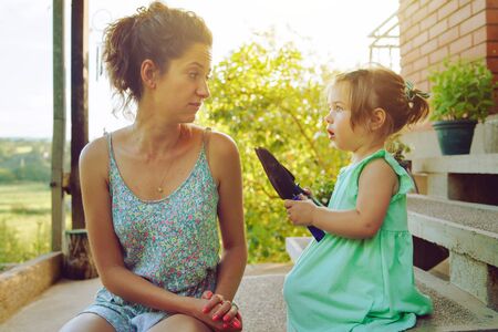 Young mother and daughter holding gardening tools in summer day sitting on the steps in front of their homeの写真素材