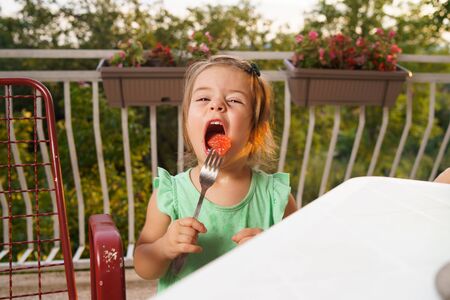 Portrait of little small girl blonde hair eating fruits watermelon in summer day by the table on her balconyの写真素材