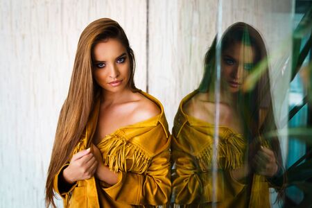 Portrait of Beauty fashion model posing in front of the wall looking at the camera beautiful young woman girl with long hair with reflection in the windowの写真素材