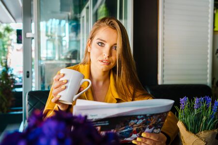 Portrait of young beautiful woman at cafe restaurant reading news newspaper and having a cup of coffee or teaの写真素材