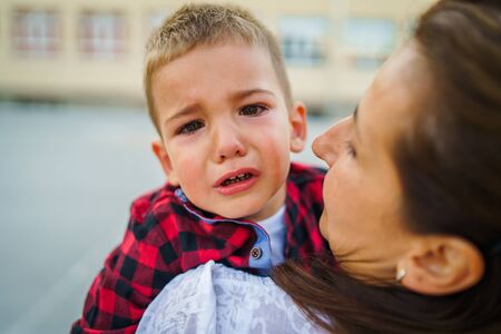 Mother or grandmother is holding small little boy child son crying in summer day outdoorの写真素材