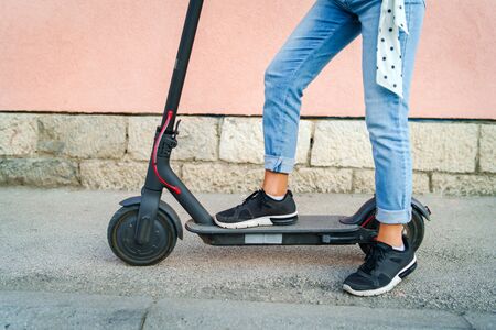 Close up on woman legs feet standing on the electric kick scooter on the pavement wearing jeans and sneakers in summer dayの写真素材