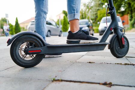 Close up on woman legs feet standing on the electric kick scooter on the pavement wearing jeans and...