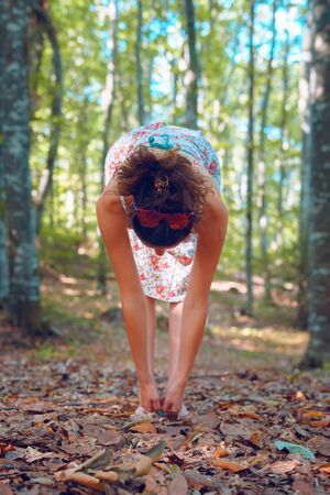 Young woman in summer dress in the forest woods in autumn doing yoga stretching in peace balance spirituality and nature conceptの写真素材