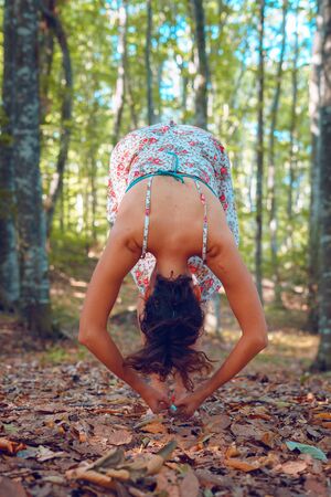 Young woman in summer dress in the forest woods in autumn doing yoga stretching in peace balance spirituality and nature conceptの写真素材
