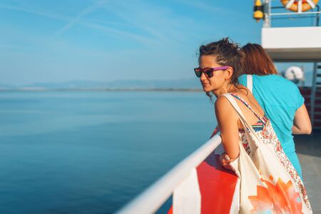 Back view of young woman standing on the deck of the ship or ferry boat in sunny day on vacation...