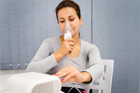 Portrait of adult woman using steam vapor inhaler nebulizer doing aerosol inhalation medicine treatment at home or hospital flu and asthma bronchitis virus healingの写真素材