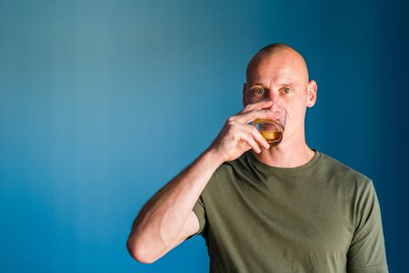 Portrait of young handsome man with short hair holding a glass of whiskey or brandy alcohol drink...