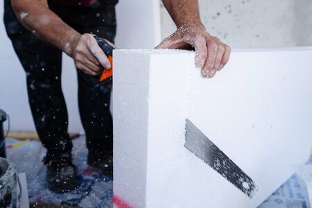 Construction worker using the hand saw to cut the  insulation panel table at the construction site in the insulating renovation procedureの写真素材