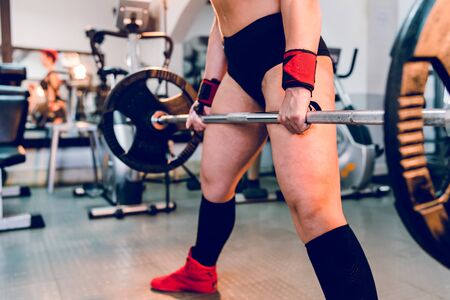 Young caucasian woman working out at gym training deadlift dead lifting weights holding barbel with weight plates strength power female midsectionの写真素材