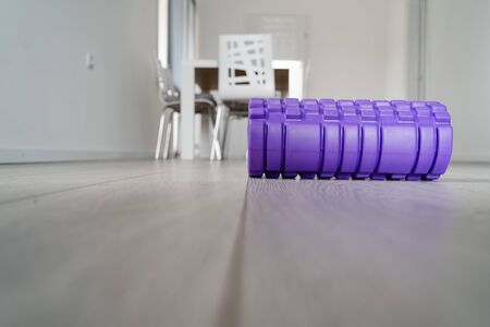 Purple textured foam roller for body massage on the light white wooden floor at home in front of the...