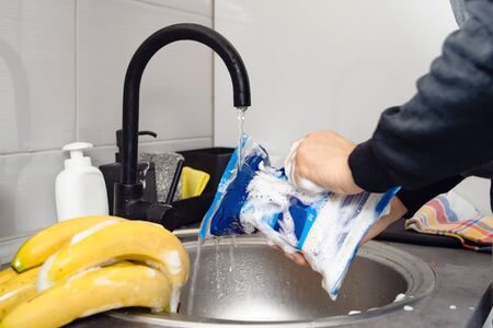 Side view on hands of unknown caucasian man person holding a rice bag under sink tap washing food with soap cleaning disinfection in water to disinfect from viruses or pollution at home in kitchenの写真素材