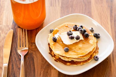 Top angle view on white plate on the wooden board table with pancakes and butter blueberries over...
