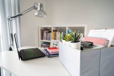 Box with personal items stuff packed on the white table in the office or home in day by the laptop...