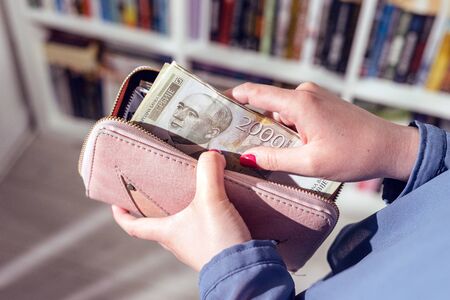 Close up on serbian dinar RSD money banknotes in hand of unknown caucasian woman holding putting wallet after receiving payment loan help financial aid support due economic recession crisis top viewの写真素材