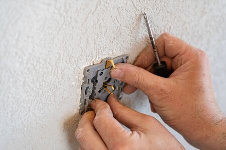 Close up on hands of caucasian man electrician holding screwdriver working on the plug electrical outlet residential electric system installing AC power socket on gray wall at home repair close upの写真素材