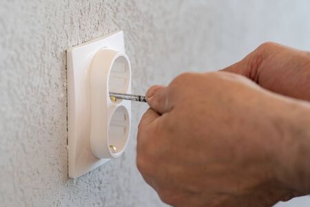 Close up on hands of caucasian man electrician holding screwdriver working on the plug electric on...