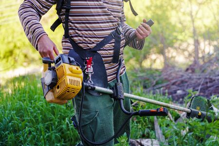 Midsection of unknown Young caucasian man farmer gardener standing in the field with string trimmer...