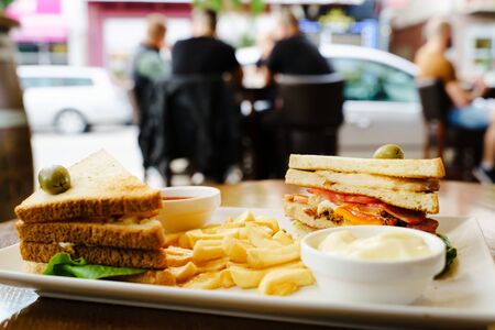 Club sandwich in a plate in restaurant on the table with fresh french fries chips and ketchup and mayonnaise ready for breakfast or lunch front viewの写真素材