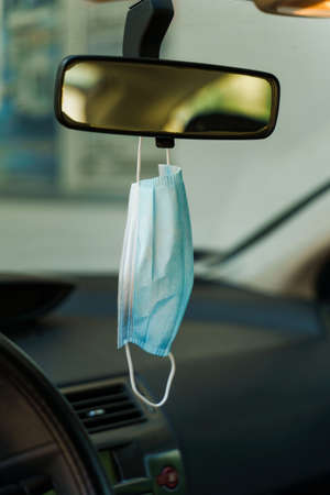 Medical protective face mask in car on the rearview mirror in day - Covid-19 pandemic protection on rear view in the vehicle - coronavirus epidemic new normal prevention conceptの写真素材