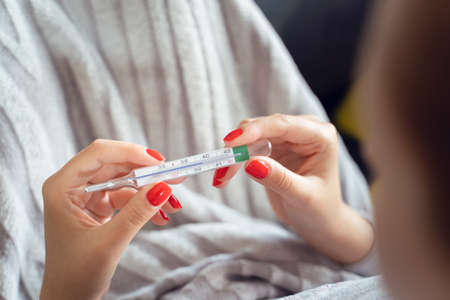 Close up on hands of unknown caucasian woman holding thermometer while lying in bed - Adult female...