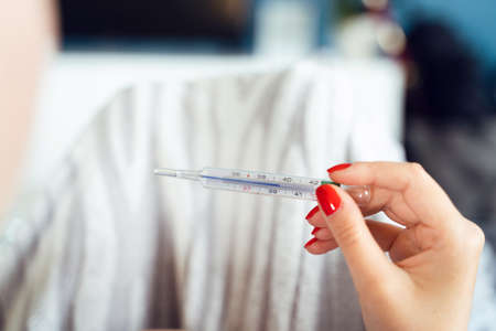 Close up on hands of unknown caucasian woman holding thermometer while lying in bed - Adult female...