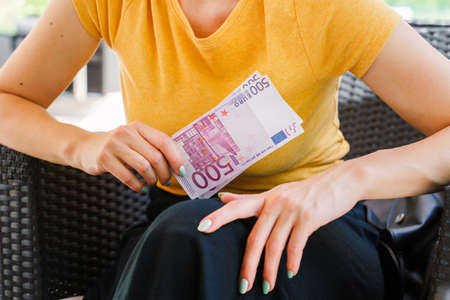 Close up on midsection of unknown caucasian woman holding 500 euro banknotes money while sitting in day - Paying earnings salary wealth conceptの写真素材