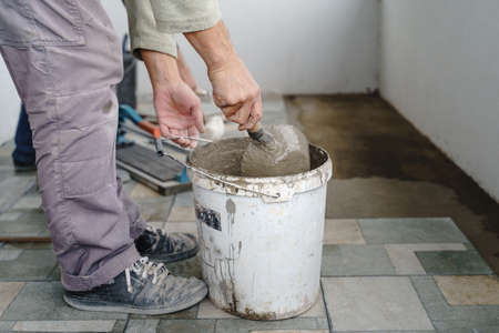 Close up on bucket with adhesive construction glue cement and unknown craftsmen holding tool in hand...