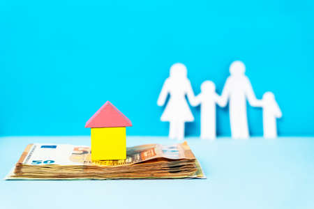 Close up on wooden house on top of the pile or money eur banknotes with family in background with copy space - house buying home insurance and savings real estate loan conceptの写真素材