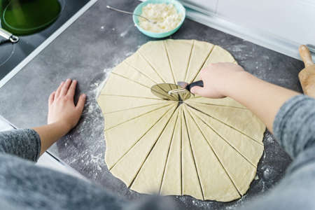 Top angle view on hand of unknown caucasian woman cutting prepared dough to make croissants on the kitchen counter at home - domestic traditional recipe homemade cuisineの写真素材