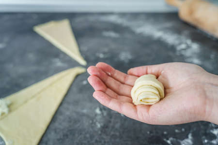 Close up on hand of unknown caucasian woman holding raw dough croissant with cheese over the kitchen counter at home - traditional recipe domestic homemade food healthy eating conceptの写真素材