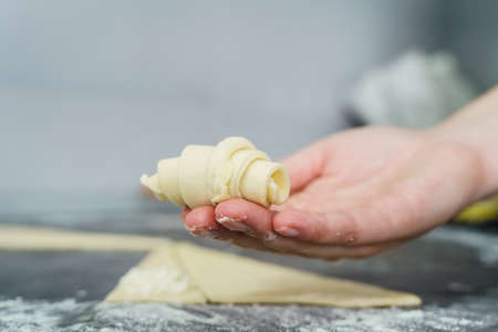 Close up on hand of unknown caucasian woman holding raw dough croissant with cheese over the kitchen counter at home - traditional recipe domestic homemade food healthy eating conceptの写真素材