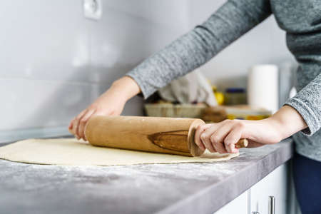 Close up on hands of unknown caucasian woman preparing dough paste for croissant using rolling pin...