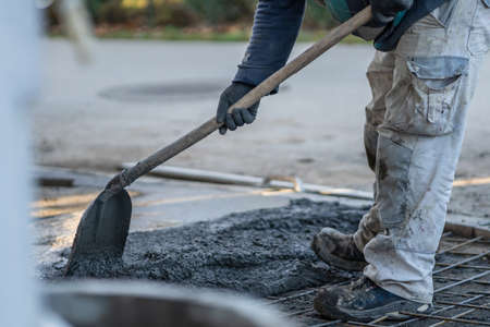 Close up on midsection of unknown worker spreading concrete cement mortar on the ground in day at construction siteの写真素材