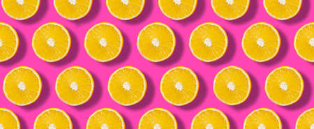 Top down view on pink abstract background with slices of ripe orange or lemon citrus in pattern - trendy minimal flat lay food summer conceptの写真素材