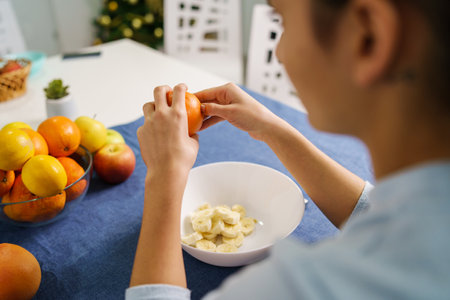 Back view on hands of unknown young woman peeling orange by the table at home - healthy eating organic vegetarian food concept copy spaceの写真素材