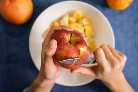 Close up on hands of unknown caucasian woman peeling red apple over the bowl on the table at home - healthy eating concept organic food homemade vegetarian or vegan meal - top viewの写真素材