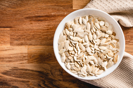 Top view on fresh salted roasted pumpkin seeds in bowl on wooden table at homeの写真素材
