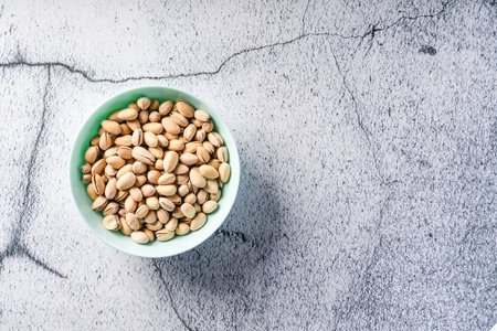 Top view on fresh salted roasted pistachios snack nuts in bowl with copy space on concrete table backgroundの写真素材