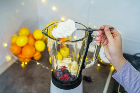 Unknown woman making organic fruit smoothie with blueberries and raspberries putting cheese cream in electric blender on the kitchen counter - healthy eating concept copy spaceの写真素材