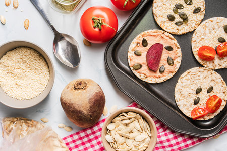 Crispy puffed rice cakes on table hummus spread and tomato and beet vegetables and sesame pumpkin...