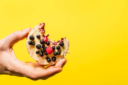 Hand holding crispy puffed rice cake with fresh fruit blueberries raspberries in front of the the yellow background - healthy organic vegetarian or vegan breakfast gluten free copy spaceの写真素材