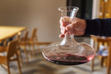 Close up on hand of unknown caucasian man holding decanter with red wine in the hall at home or...