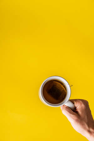 Top view on hands holding cup of tea in front of yellow backgroundの写真素材